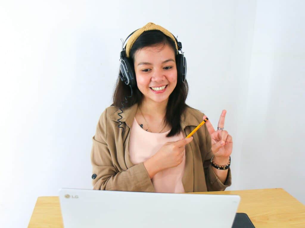 A teacher pointing to their fingers with a pencil as they give a secure online class to their laptop, sat down at their desk.